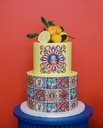 Two-tiered cake with colorful design and fruit on top against a red background