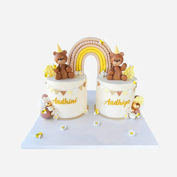 Two small cylindrical cakes with teddy bears and a rainbow on top, on a white background.
