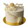 White birthday cake with gold accents and 'Happy Birthday' topper on a white background